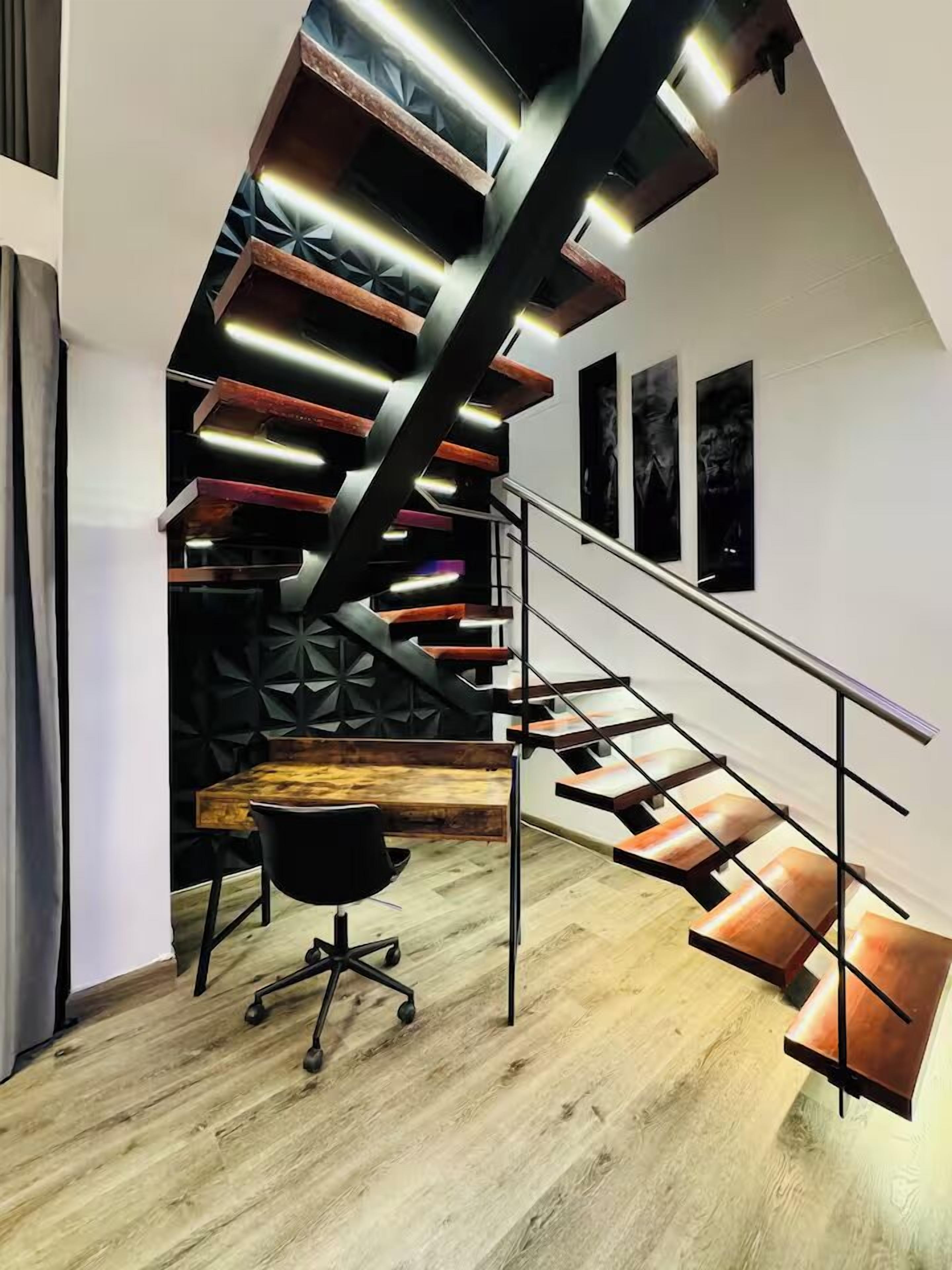 Una escalera moderna con escalones de madera y barandillas de metal, que desciende a un nivel inferior.