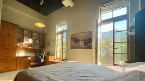A bedroom with a large bed, wooden furniture, a desk, and a window with a view of greenery. - Manitou Incline Retreat

 (Manitou Springs)