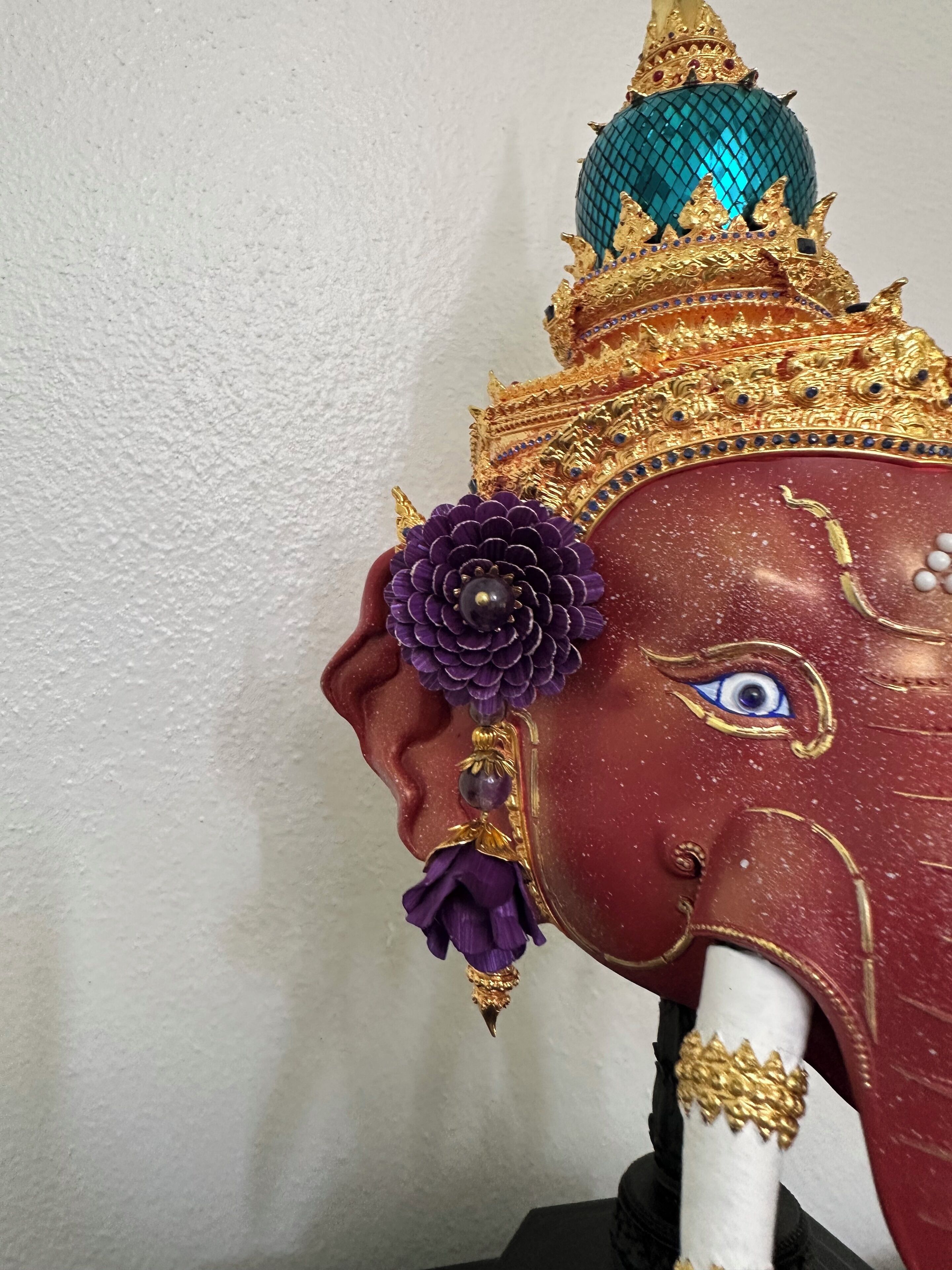 A statue with a detailed head, featuring a golden crown, a blue and green dome, and a purple flower.