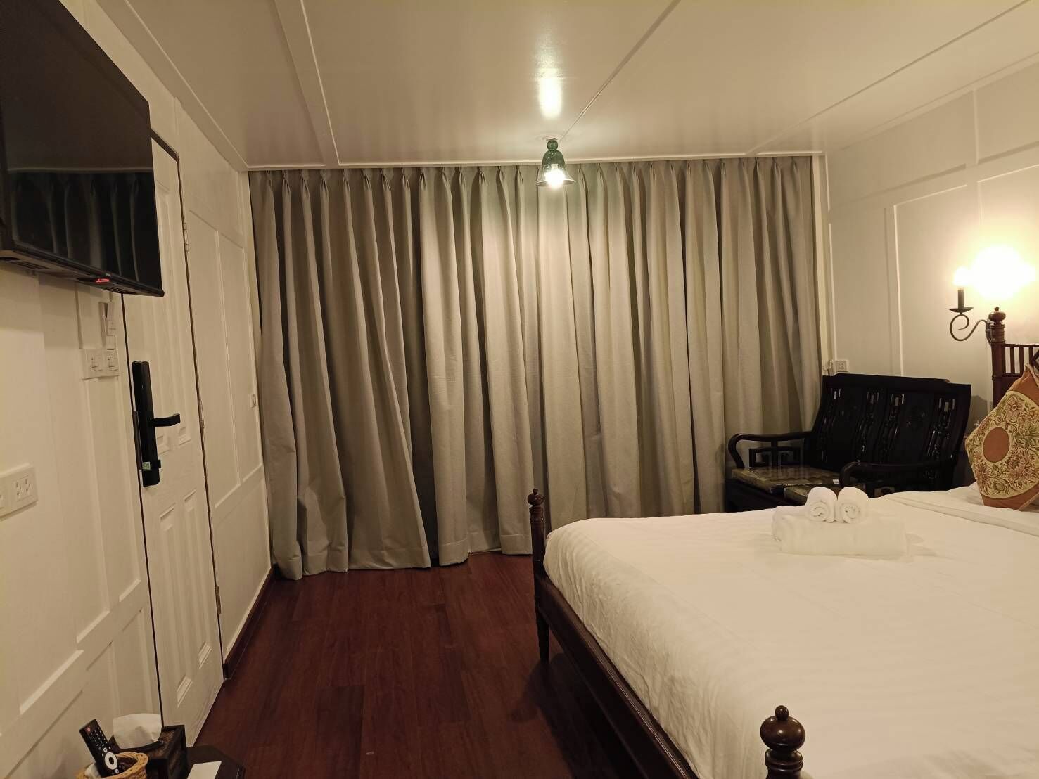 Et hotelværelse med seng, gardiner, en stol, et skrivebord og et fjernsyn.