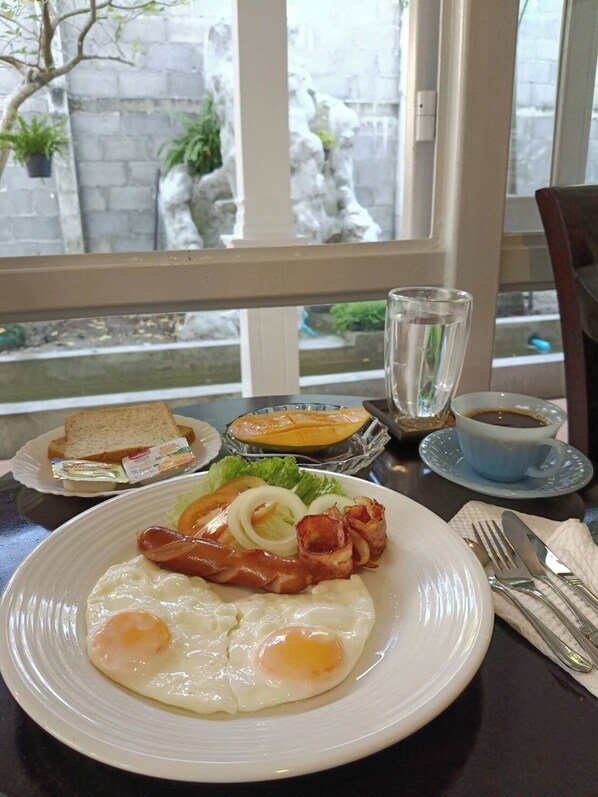 A breakfast plate with eggs, bacon, toast, and a glass of orange juice. - Baan Debtida (Bangkok)