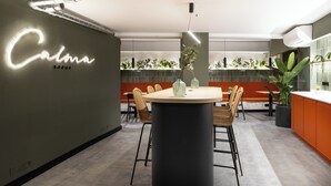 A modern interior with a round table, chairs, a neon sign, and indoor plants. - Calma Rooms by Charming (Madrid)