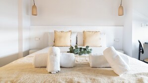 A neatly made bed with white linens and two pillows, a bedside table with a lamp, and a chair. - Calma Rooms by Charming (Madrid)