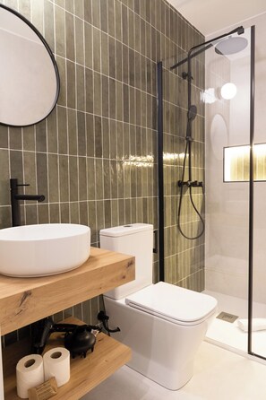 A modern bathroom with a round mirror, white sink, and a glass-enclosed shower area. - Calma Rooms by Charming (Madrid)