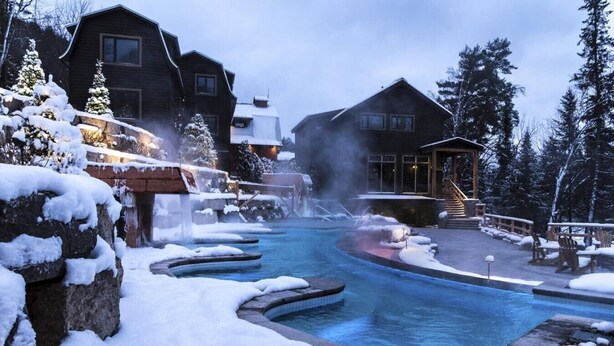 A heated outdoor pool with snow-covered steps and a wooden building in the background.