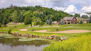 A golf course with a pond, sand bunkers, and a lodge with a deck overlooking the course.