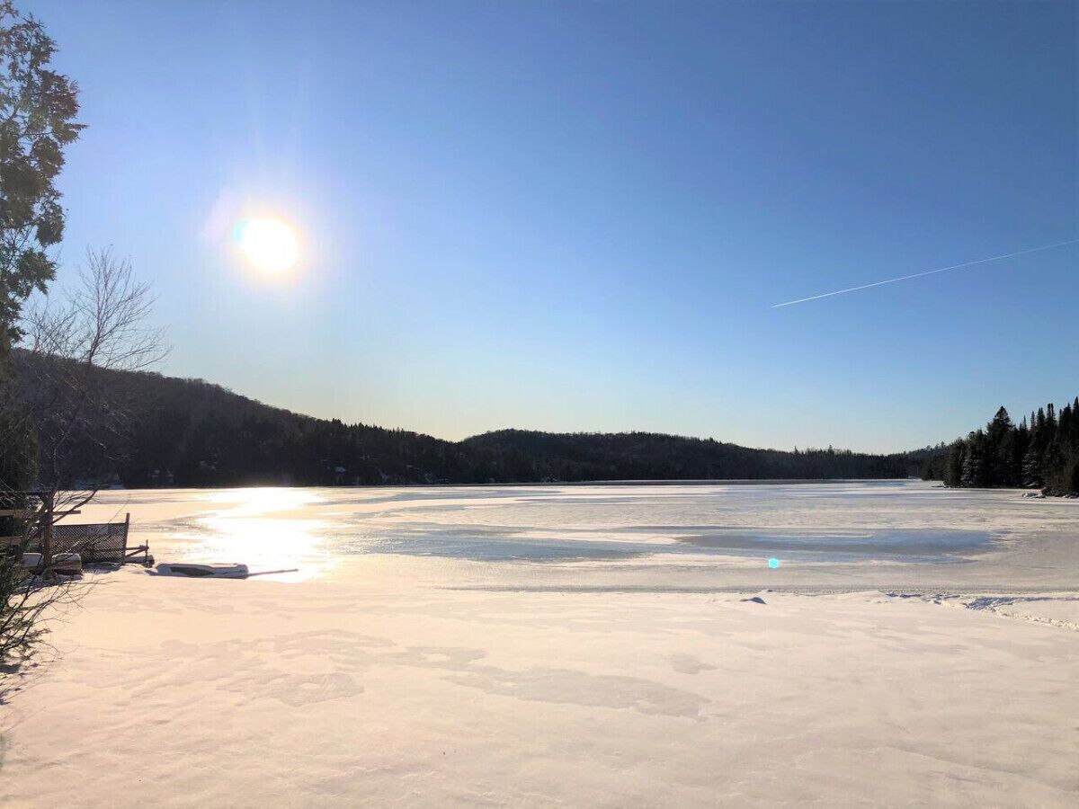 Un lac gelé, sous un ciel dégagé, avec des arbres qui se dessinent à l’horizon.