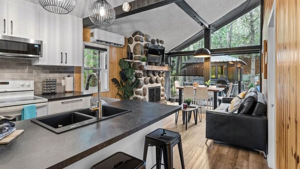 Una cocina moderna con chimenea de piedra, un comedor con mesa y sillas de madera, y un sofá de cuero negro.