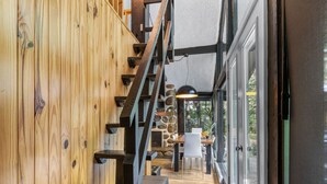 Una escalera de madera conduce a un comedor con chimenea de piedra, una mesa y sillas.