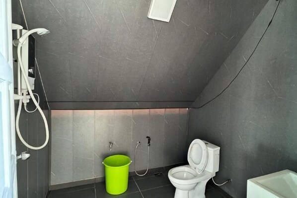 Ein Badezimmer mit Toilette, Dusche und einem grünen Eimer.