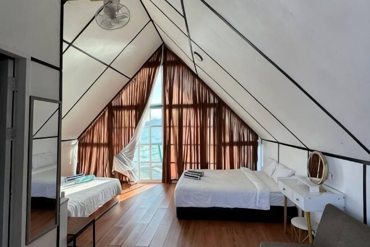 A bedroom with a sloped ceiling, a bed, a bedside table, a chair, and a window with curtains.