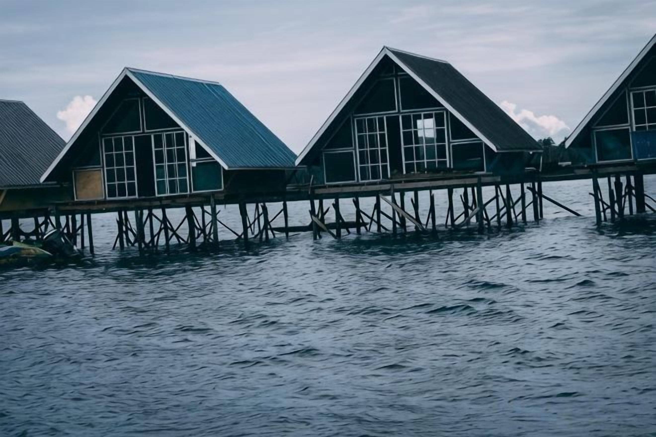 Overwater bungalows with a simple, functional design, connected by a wooden walkway over calm water.