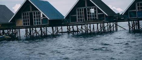 Overwater bungalows with a simple, functional design, connected by a wooden walkway over calm water.