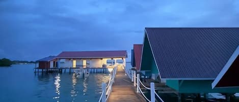A wooden pier leading to overwater bungalows with a calm water body in the background.