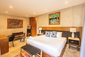 A hotel room with a large bed, a desk, a chair, and two paintings on the walls.