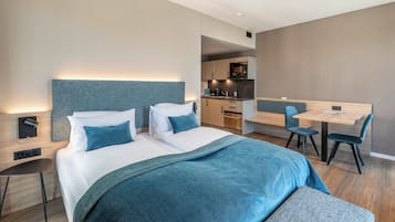 Quarto de hotel moderno com uma cama grande, uma mesa de escritório e uma cozinha compacta.