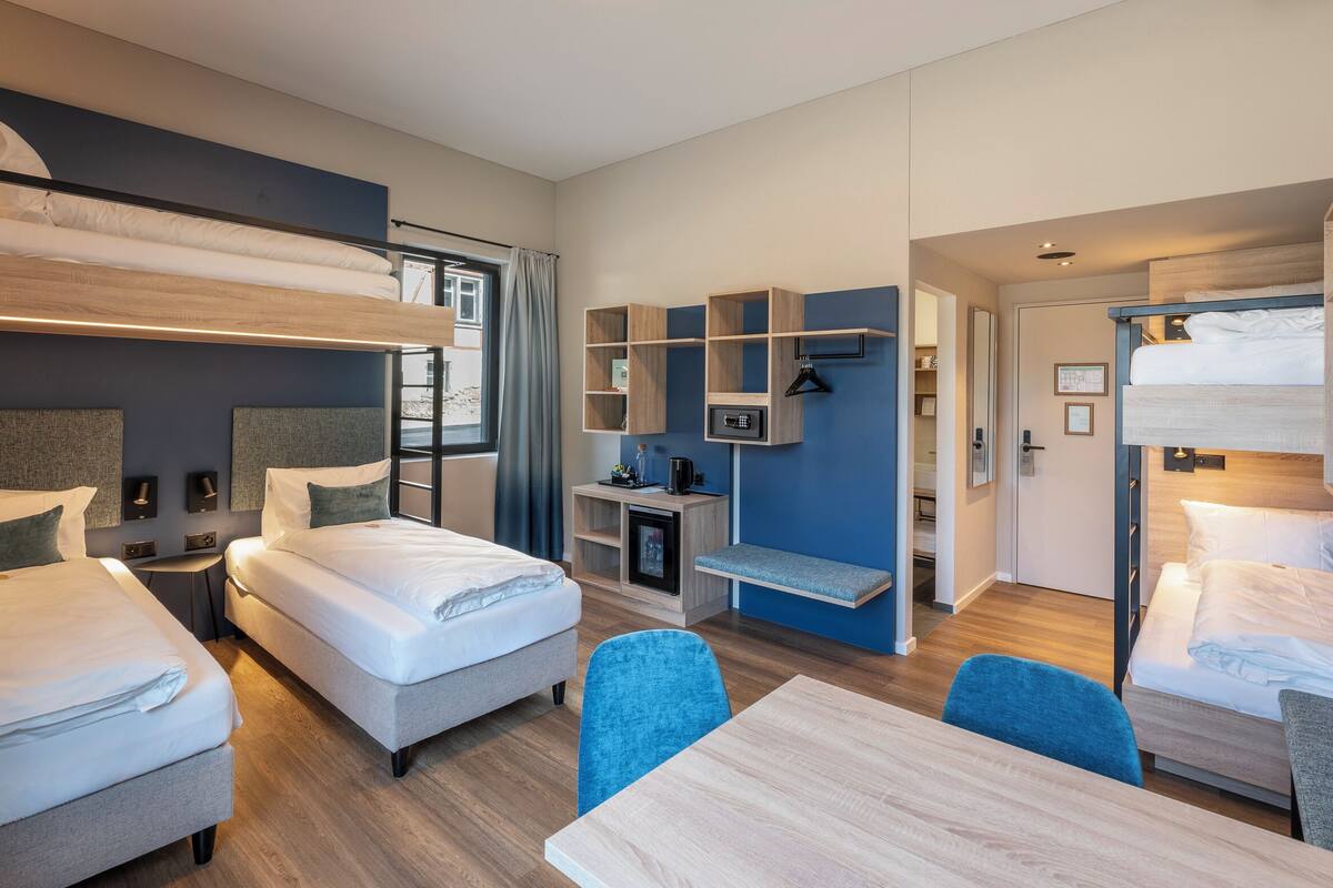 A modern hotel room with bunk beds, a desk, and a seating area.
