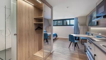 A modern kitchen with wooden cabinetry, a dining area with blue chairs, and a large window providing a view of the outdoors.
