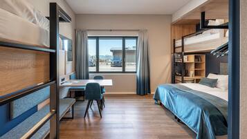 Quarto de hotel compacto com beliche, escrivaninha com cadeira e uma janela grande que oferece vista para o exterior.