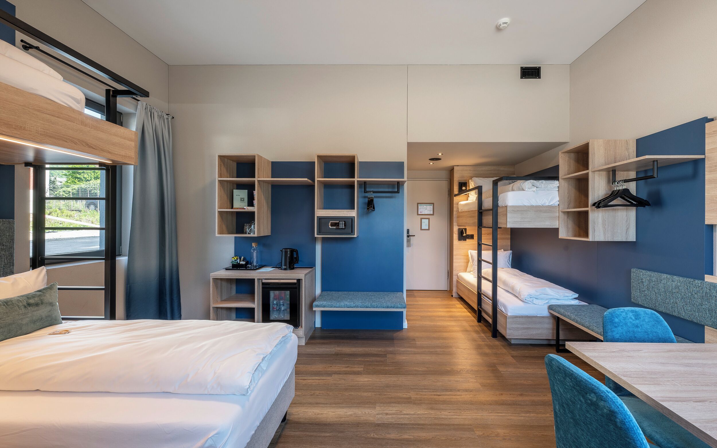A modern hotel room with bunk beds, a desk, and built-in shelving.