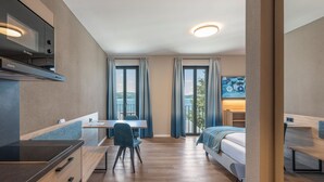 Ett modernt hotellrum med ett litet kök, ett skrivbord med en stol, en säng och en TV.