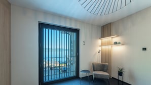 En modern hotellobby med ett stort fönster, en stol, ett litet bord och en vägghylla med dekorativa föremål.