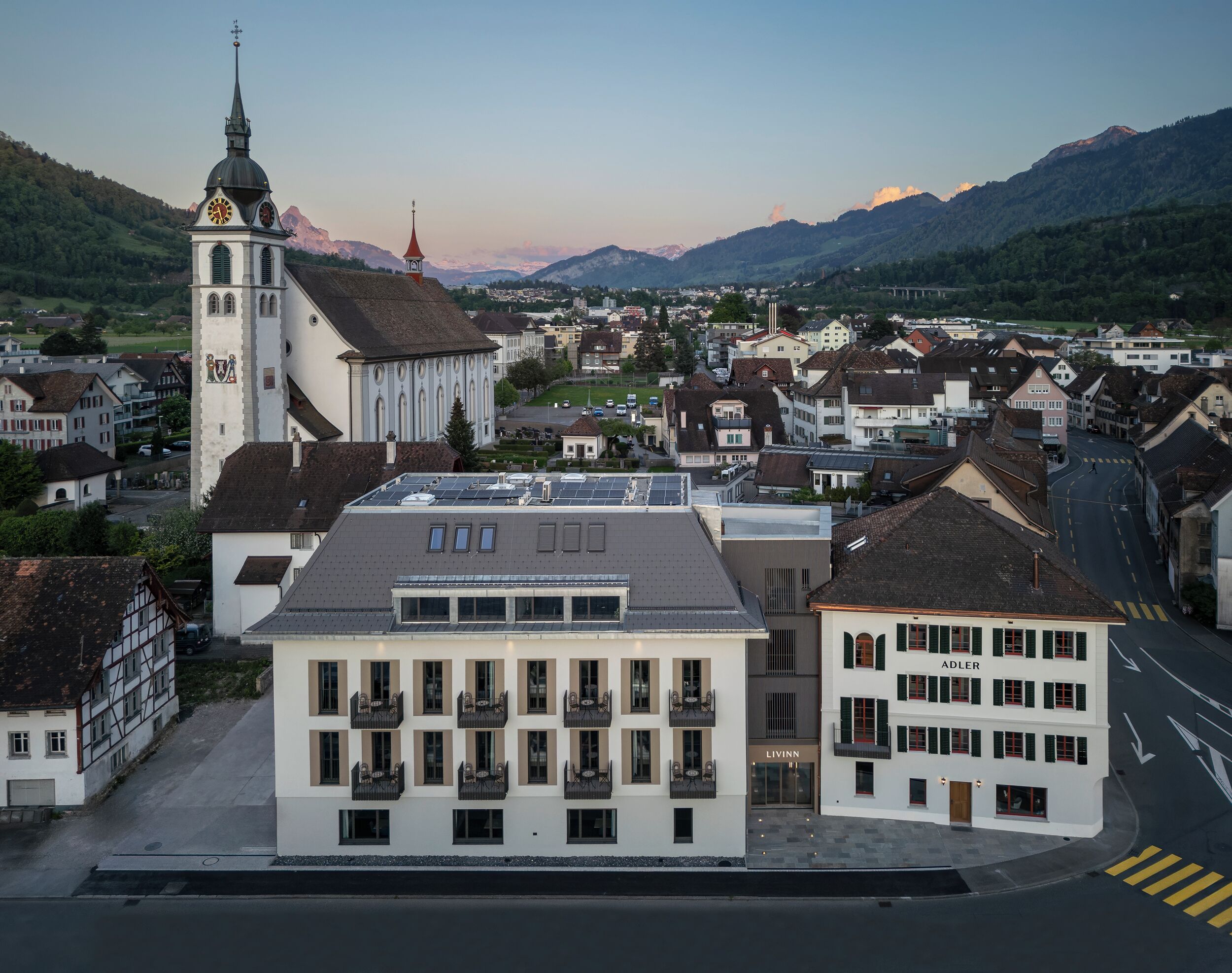 A town with a prominent church, modern buildings, and a mountainous backdrop.