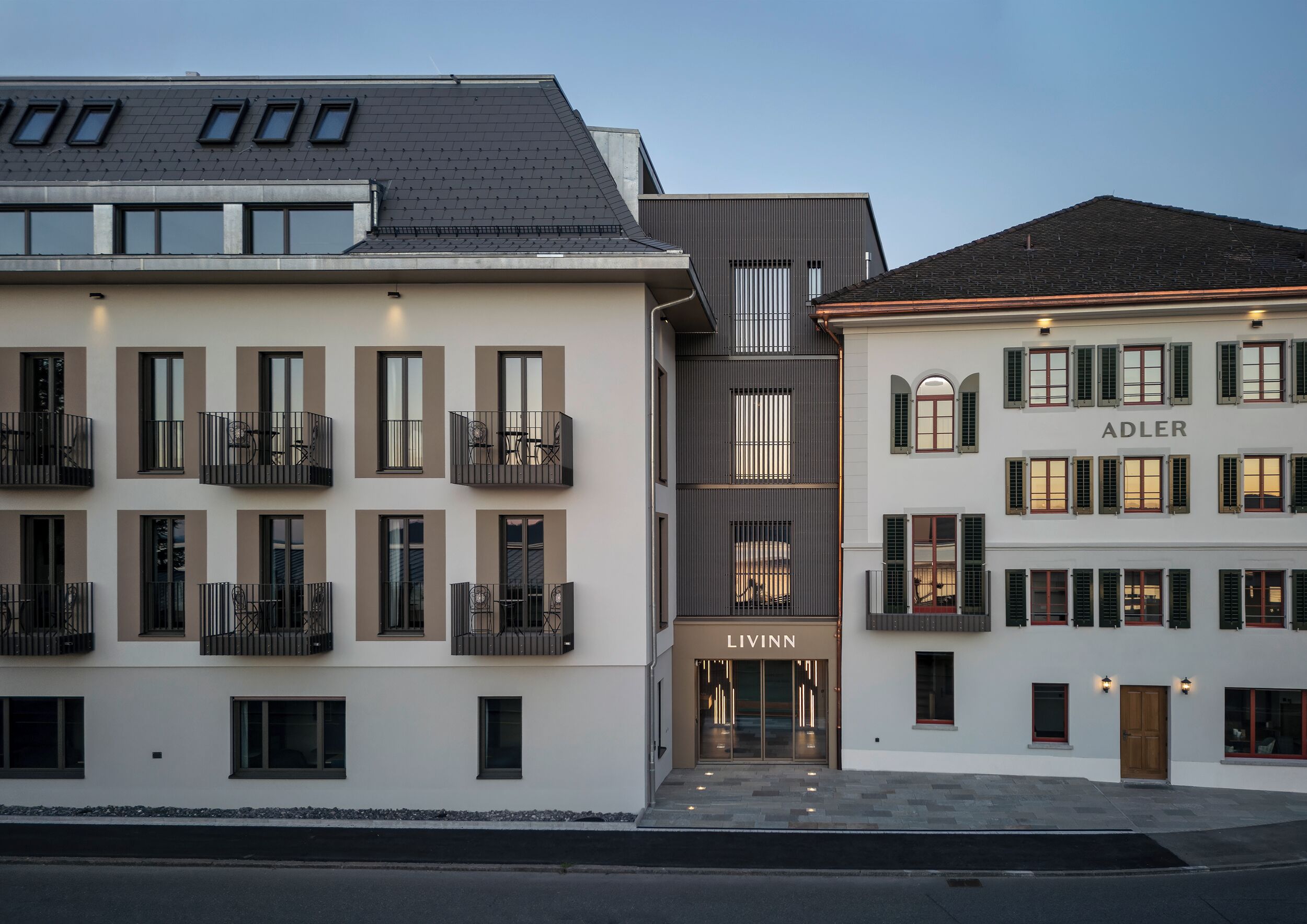 Een modern gebouw met meerdere balkons, een opvallende ingang en borden met 'ADLER' en 'LIVINN'.