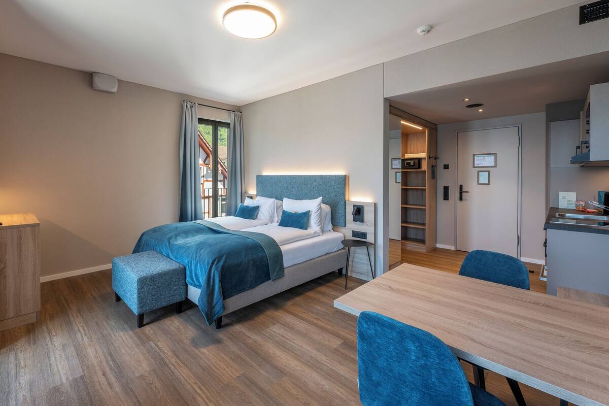 A modern hotel room with a bed, a desk, and a dining area.