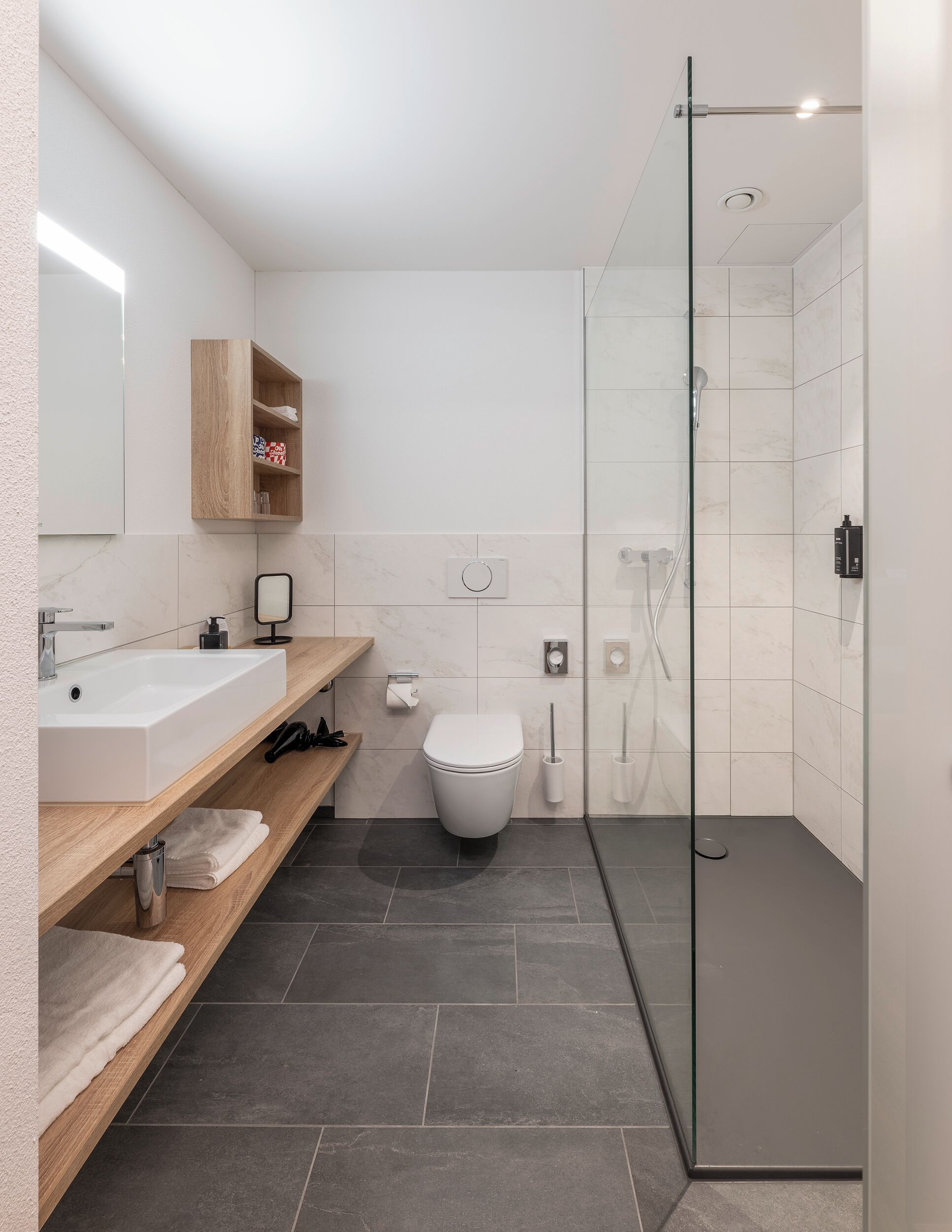 A modern bathroom with a large white sink, a toilet, and a glass-enclosed shower area.