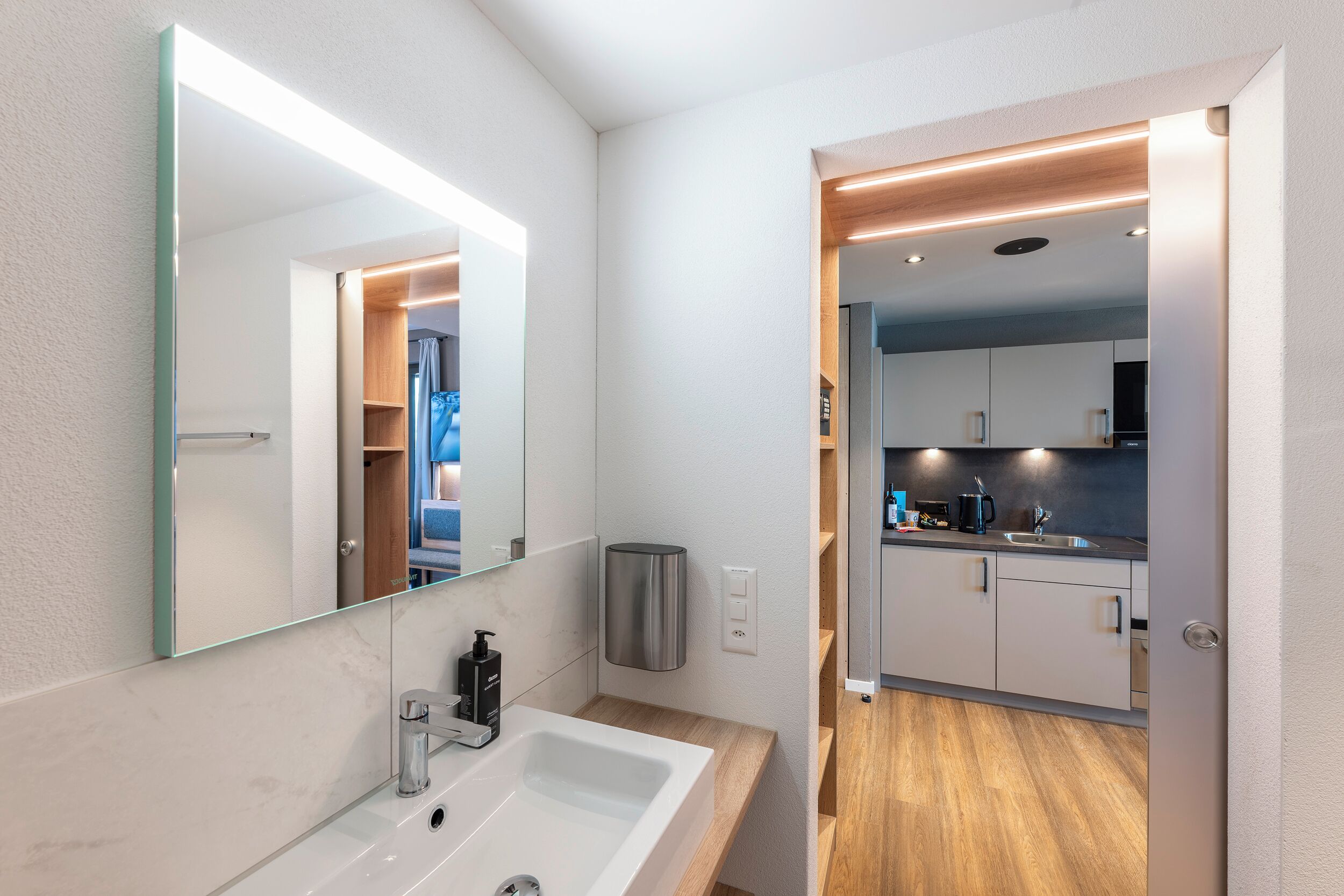 A modern bathroom with a large mirror, white sink, and wooden countertop.