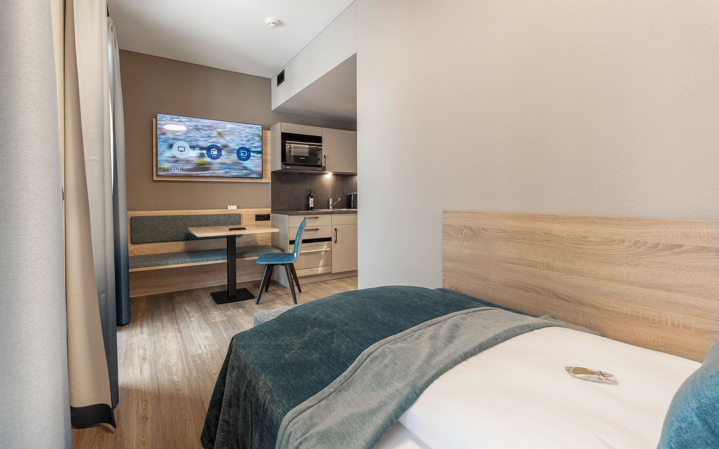 Une chambre d’hôtel comprenant un lit, un bureau avec une chaise, une télévision et une kitchenette.