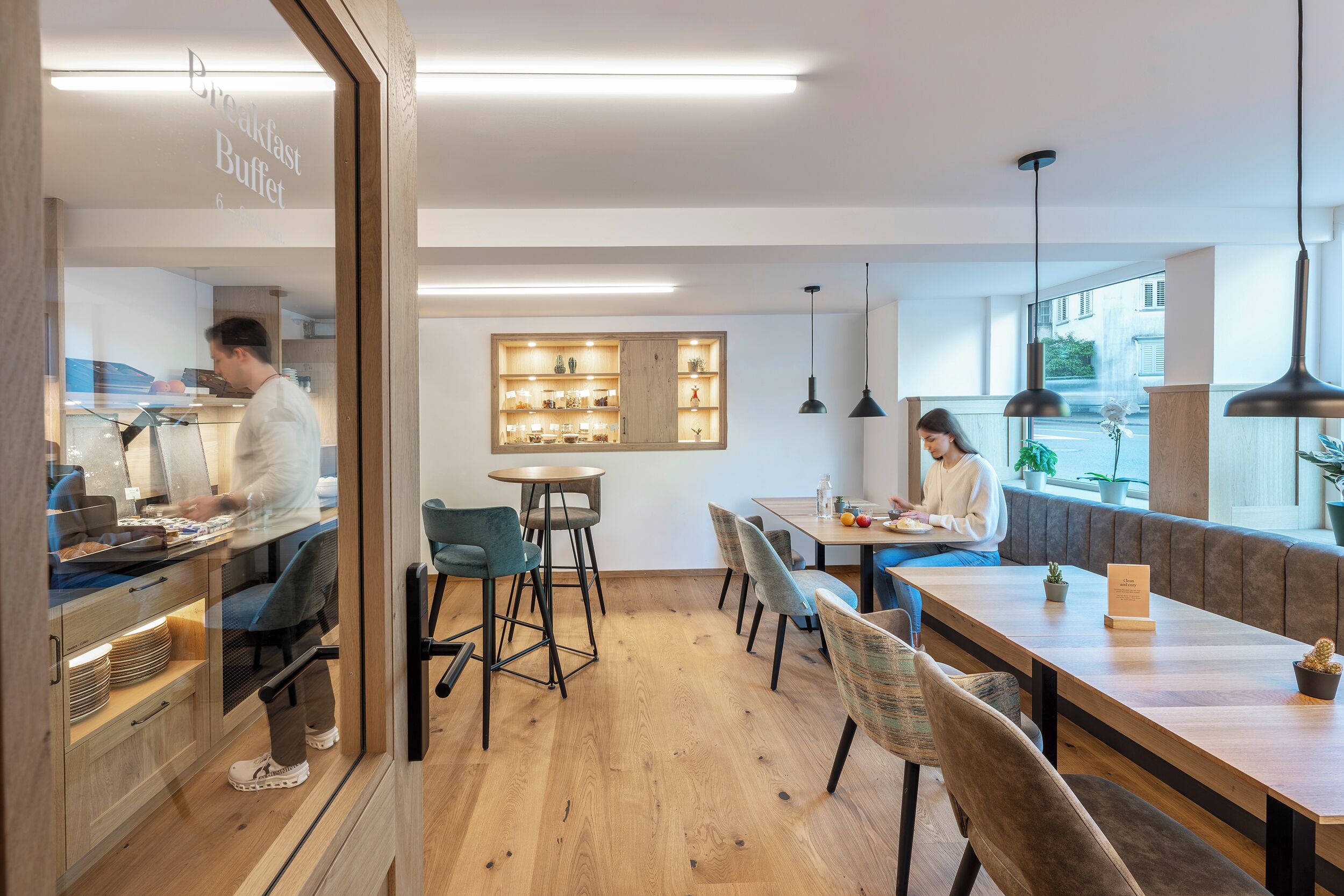 A modern restaurant with wooden floors, a breakfast buffet, and a seating area with tables and chairs.