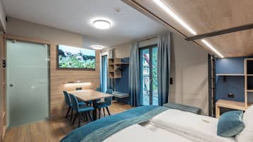 A compact room with a bed, a desk, and a chair. There is a television mounted on the wall, and a window with curtains.
