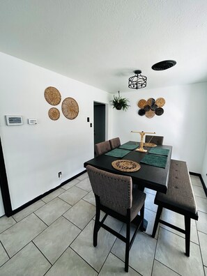A dining area with a black table, brown upholstered chairs, and a ceiling fan. - The Greenhouse Effect- central+ 4BR/2BA+ king suite+ coffee+ BBQ grill (Corpus Christi)