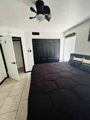 A bedroom with a large bed, a ceiling fan, a closed door, and a window with blinds. - The Greenhouse Effect- central+ 4BR/2BA+ king suite+ coffee+ BBQ grill (Corpus Christi)