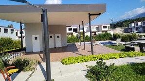 A modern building with a covered outdoor area, a swimming pool, and a well-maintained garden.