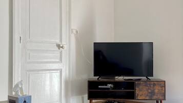 Een kamer met een houten bureau, een televisie op een houten standaard en een witte deur.