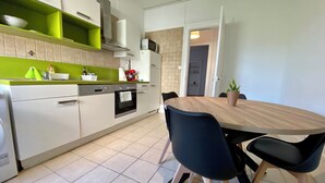A modern kitchen with white cabinets, a green countertop, and a wooden dining table with chairs.