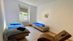 A bedroom with two beds, a wooden bench, and a radiator.