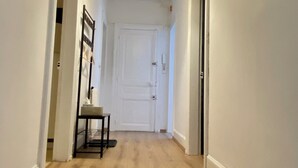A hallway with a wooden floor, a white door at the end, and a pendant light fixture.