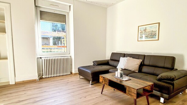 A living room with a sectional sofa, a wooden coffee table, and a radiator.