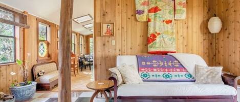 A cozy room with a wooden wall, a sofa, a patterned rug, and a large window.