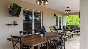 A covered patio with a wooden dining table, chairs, and a TV mounted on the wall. - Sunset Serenity in Port Charlotte (Port Charlotte)