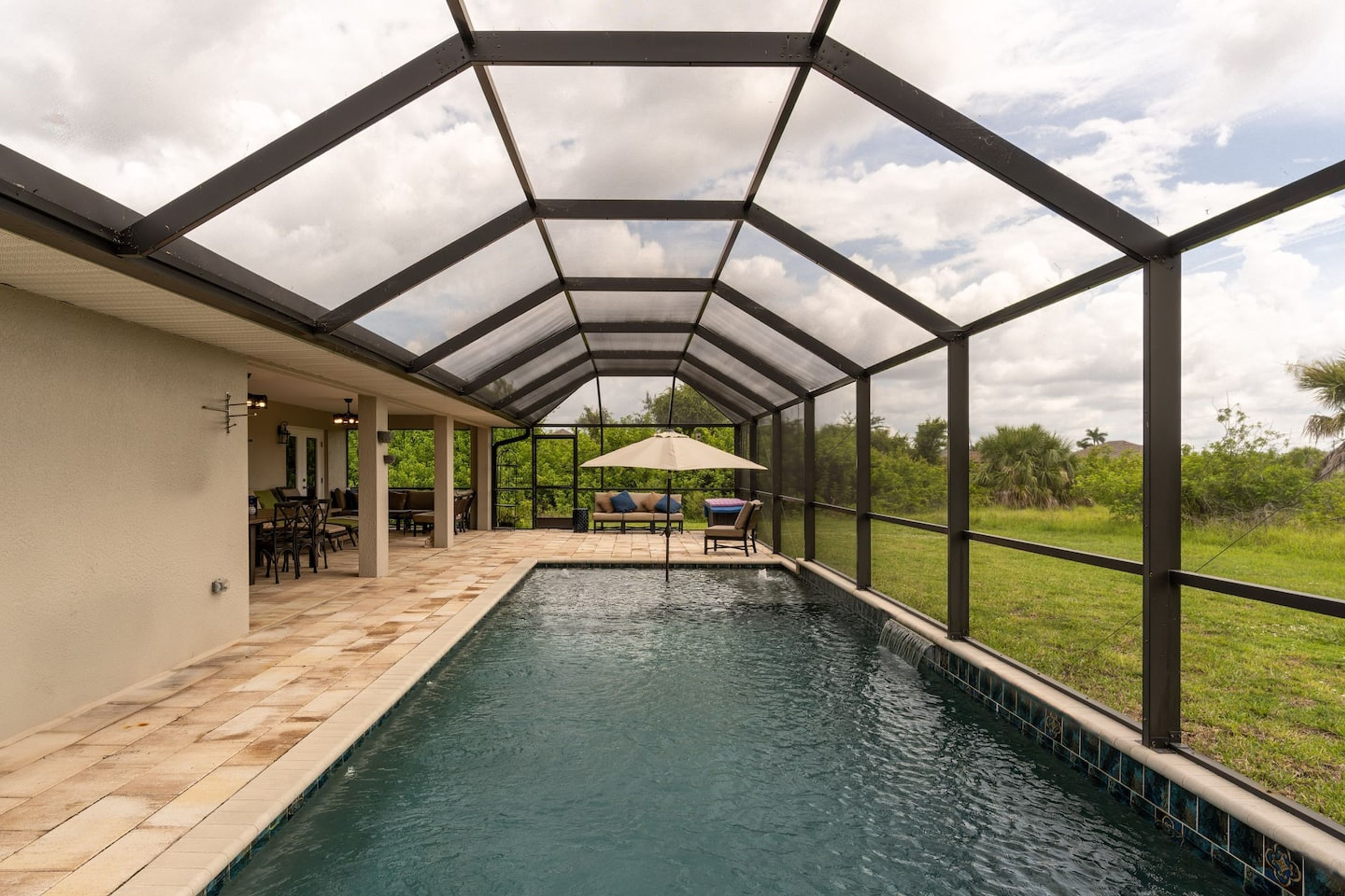 Una piscina interior con techo de cristal, rodeada por una zona de patio con mobiliario exterior.