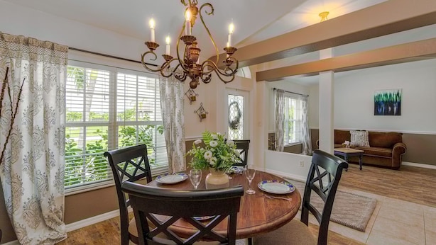 A dining area with a wooden table, four chairs, a chandelier, and a vase with flowers. - Sunset Serenity in Port Charlotte (Port Charlotte)