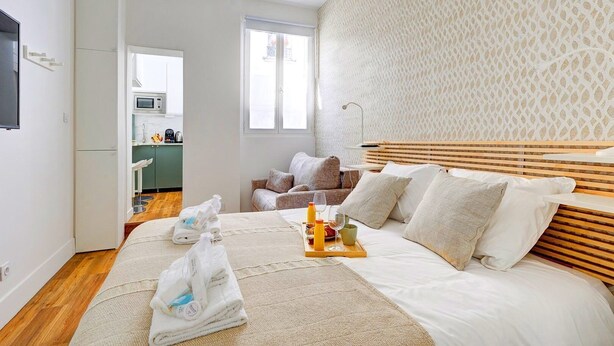 A modern hotel room with a large bed, a wooden headboard, a small kitchenette, and a view of the city. - TheBlueStay 244 - Stylish Studio - Paris 12 (Paris)