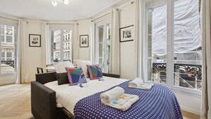 Ein Hotelzimmer mit Bett, Stuhl, Schreibtisch und einem großen Fenster mit Vorhängen.