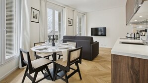 Eine moderne Küche mit Einbauofen, ein Essbereich mit rundem Tisch und Stühlen, ein graues Sofa und ein an der Wand befestigter Flachbildfernseher.
