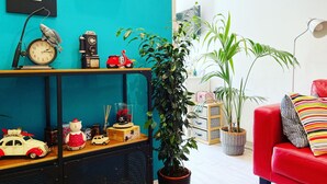 A cozy living room with a teal wall, a red sofa, a wooden shelf with various items, and a large potted plant. - Cozy Vintage Apartment in Trastevere within walking distance of downtown  (Roma)